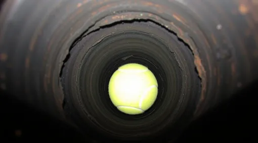 Теннисный шар/мяч лежит на дне закопанной трубы