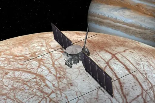 Иллюстрация зонда NASA Europa Clipper над ледяной луной Юпитера Европой. Юпитер виден справа. Космический аппарат стартовал 14 октября 2024 года и прибудет к Европе в апреле 2030 года.