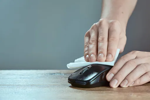 Чтобы компьютерную мышь приходилось реже чистить изнутри, регулярно протирайте ее влажной салфеткой. Мужчина протирает компьютерную мышь