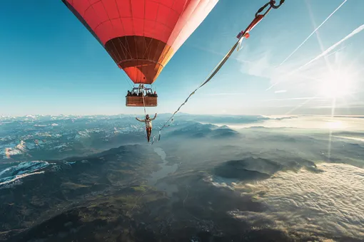 человек ходит по канату между воздушными шарами