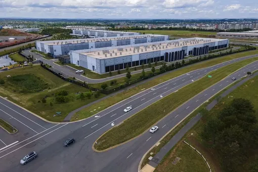 Вид сверху на центр обработки данных, состоящий из нескольких бетонных зданий. Центр обработки данных в Эшберне, штат Вирджиния, расположен рядом с автомагистралью.