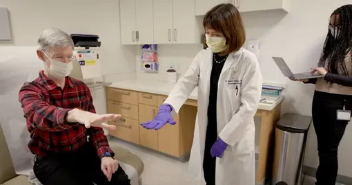 Кит Крейбил протягивает руку, повторяя движение доктора Хелены Бронте-Стюарт. После имплантации устройства адаптивной глубокой стимуляции мозга (aDBS) он сказал, что дрожь в руках исчезла «практически сразу».