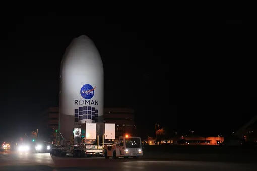 Космический телескоп NASA Nancy Grace Roman Space Telescope, помещенный в обтекатель полезного груза, перевозится из центра подготовки в ангар SpaceX на стартовом комплексе 39A в Космическом центре имени Кеннеди NASA во вторник, 25 августа 2026 года, перед соединением с ракетой SpaceX Falcon Heavy.