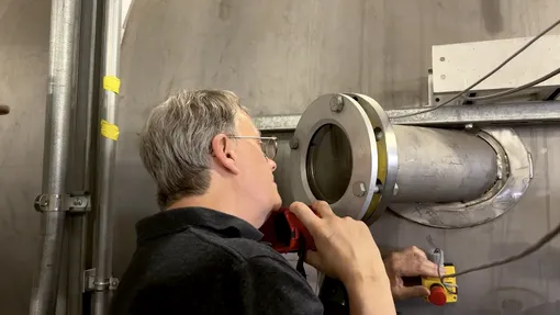 Старший научный сотрудник JPL Джеймс Полк наблюдает за работой вакуумной установки для конденсируемого металлического топлива (CoMeT) в Лаборатории электрических двигателей JPL, где в феврале 2026 года проходили испытания прототипа мощного электрического двигателя, разработанного его командой.