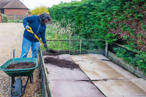Женщина засыпает картон почвой для подавления роста сорняков Женщина засыпает картон почвой для подавления роста сорняков