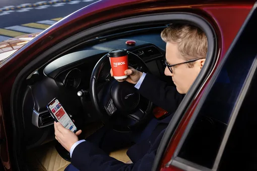 водитель держит в руке стакан с брендовой оклейкой