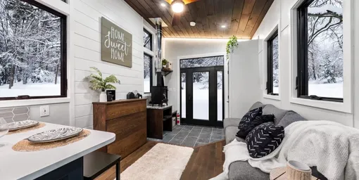 Фото Retirement Retreat от Backcountry Tiny Homes изнутри: гостиная с дровяной печью, справа диван, слева столик и место для телевизора, впереди застекленные двери Фото Retirement Retreat от Backcountry Tiny Homes изнутри: гостиная с дровяной печью, справа диван, слева столик и место для телевизора, впереди застекленные двери